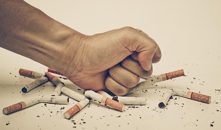 A foto mostra uma mão esmagando um monte de bitucas de cigarros. Parar de fumar ajuda a prevenir contra o Alzheimer