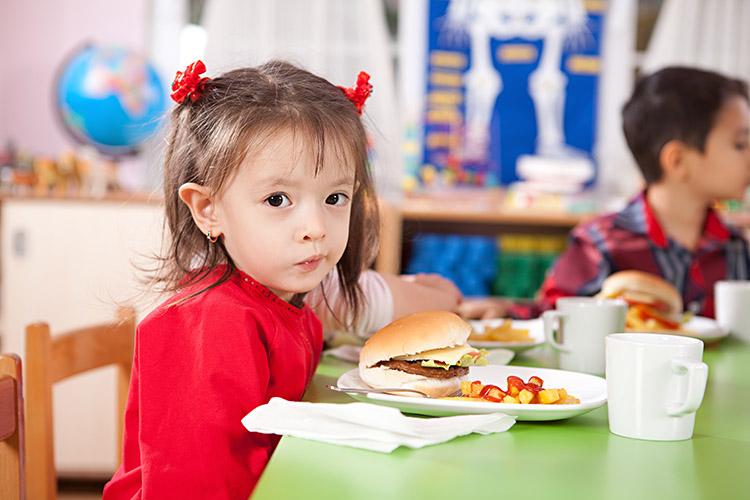 menina-pequena-sentada-mesa-comendo-hamburguer-alimentos-ruins
