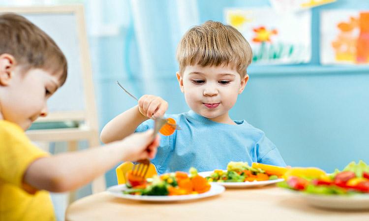 meninos-mesa-sentados-comendo-legumes-talheres-comida-infantil