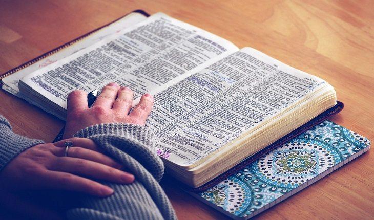 mulher com blusa de frio apoiando as mãos sob uma bíblia aberta em cima de uma mesa