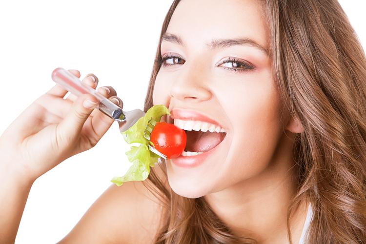 Mulher mordendo um garfo contendo alface e tomate