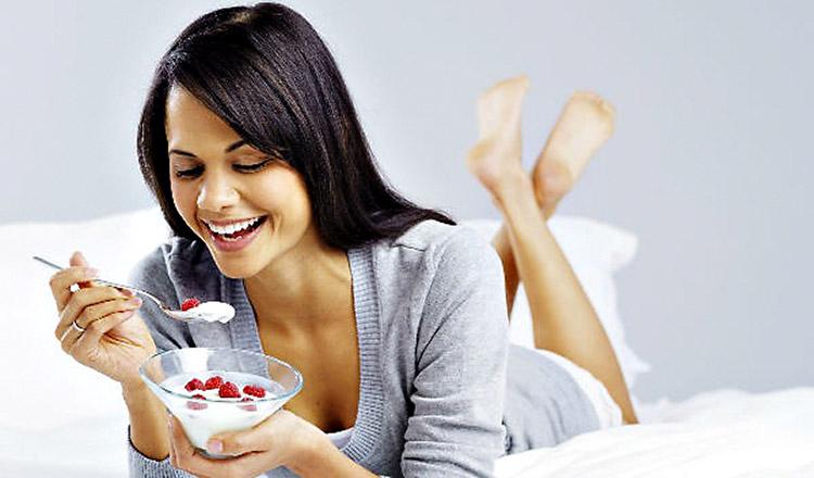 mulher-deitada-cama-comendo-iogurte-frutas