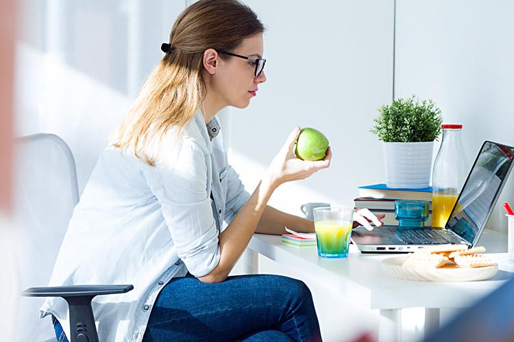 mulher-sentada-computador-comendo-maca-verde