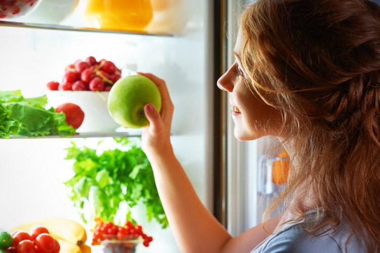 mulher pegando uma maçã verde na geladeira