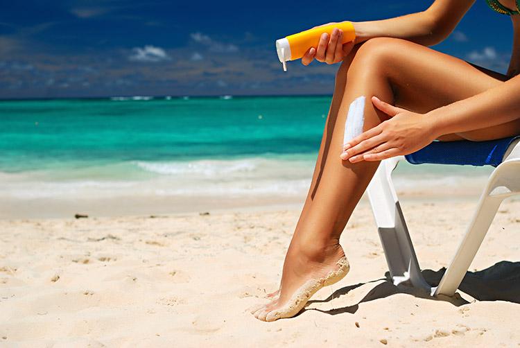 mulher-sentada-praia-protetor-solar-perna