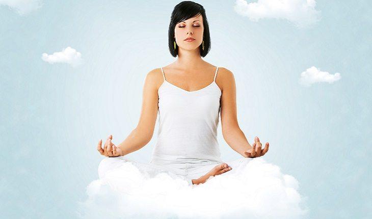A foto mostra uma mulher com camiseta cavada branca sentada em uma nuvem meditando