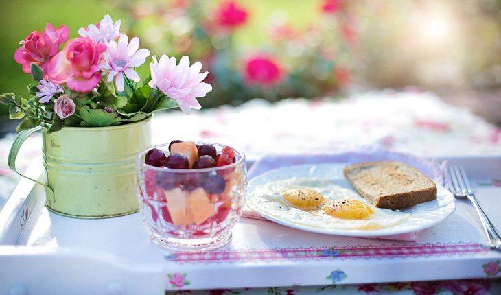 Dicas para relaxar. Na foto, uma mesa de café da manhã com flores, frutas, ovos fritos e torradas