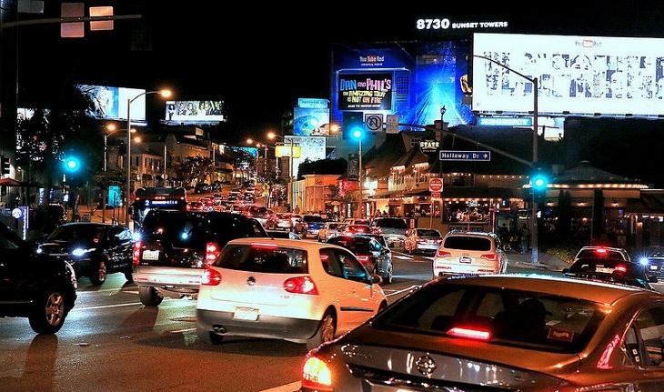 vários carros na avenida Sunset Boulevard, na altura da Sunset Strip, durante a noite.