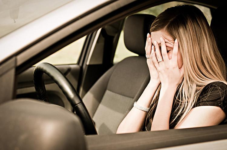 mulher no carro com a mão no rosto, estressada dirigindo