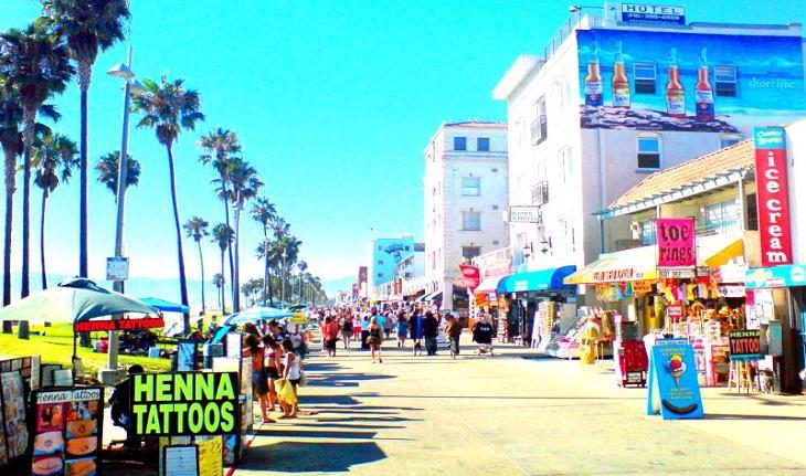 Calçadão de Venice Beach, com várias pessoas passeando, lojinhas e tatuadores.
