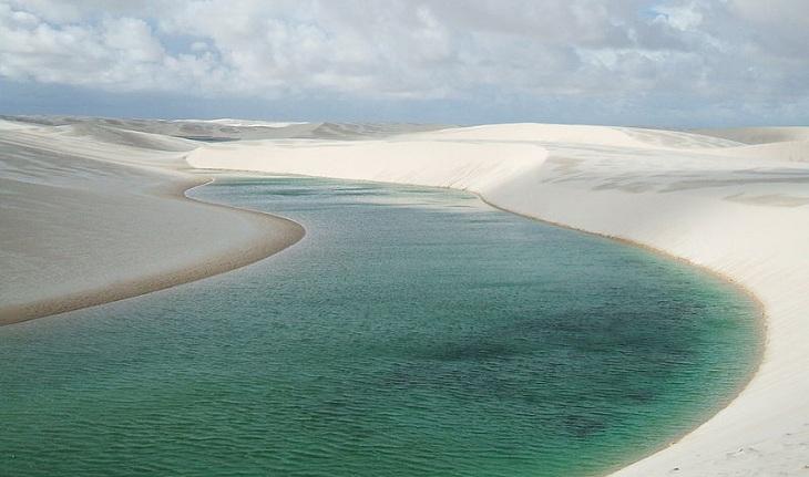 vista de dunas dos Lençóis Maranhenses, com uma faixa de água esverdeada cortando-as.