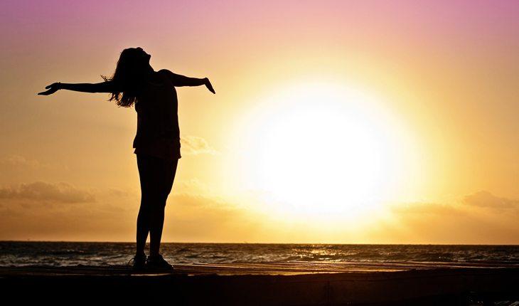 Na foto há uma mulher dançando no pôr do sol