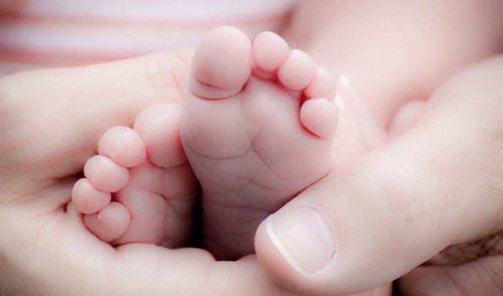 Na imagem, uma mão segura os pés do bebê rescém-nascido. Dezembro vermelho.