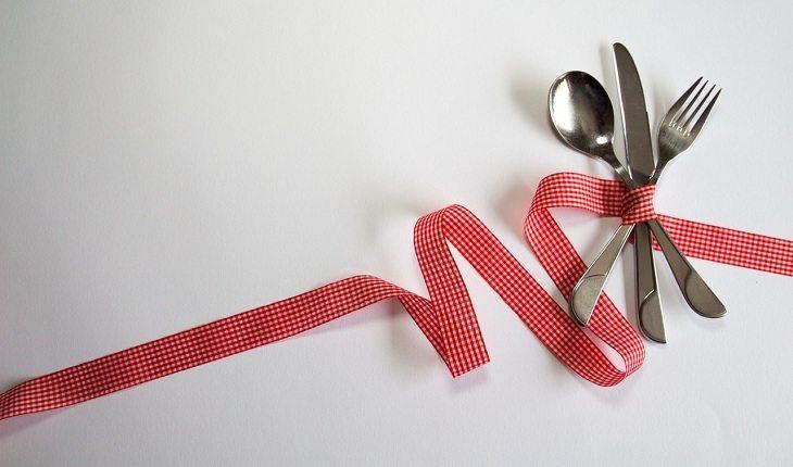 Na imagem, uma fita vermelha amarra um garfo, uma faca e uma colher de prata. Dezembro vermelho.