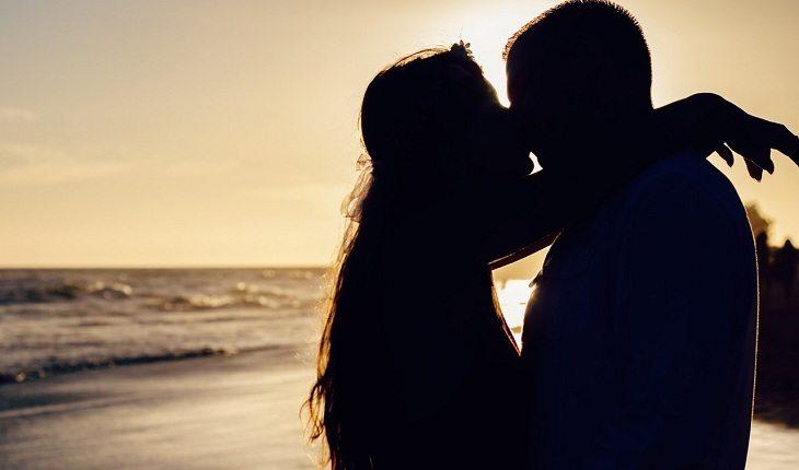 Na imagem, o casal está se beijando na praia ao por do sol. Dezembro vermelho.
