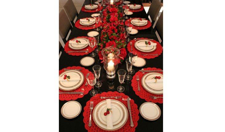 mesa de natal com toalha escura e sousplat vermelhos e redondos com pratos brancos em cima