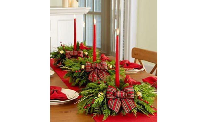 enfeites de centro de mesa de natal com plantas, laços vermelhos e velas vermelhas no centro