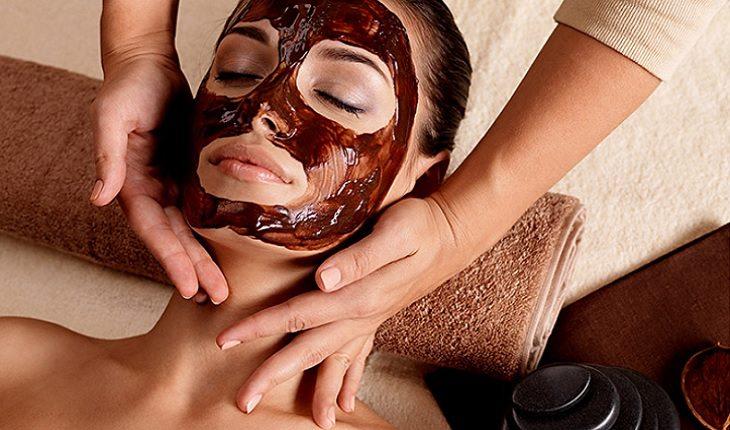 A foto mostra uma mulher fazendo chocolaterapia com uma camada de chocolate na face