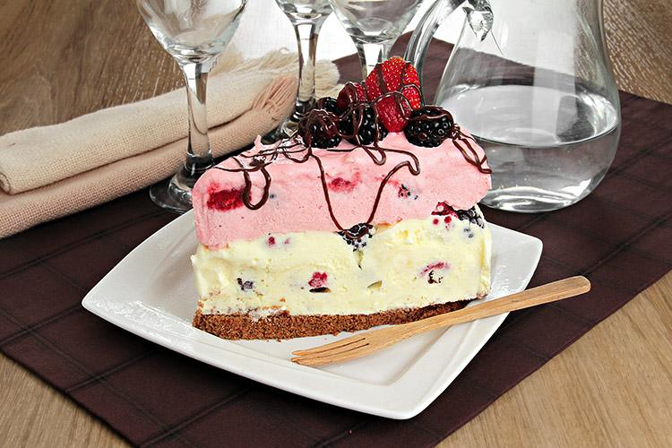 Fatia de Bolo de sorvete e frutas vermelhas em um prato quadrado branco.