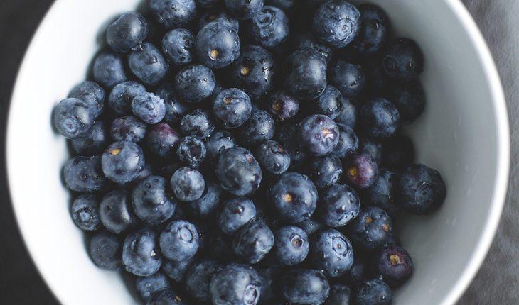 Na foto há blueberrys em um potinho branco e redondo.
