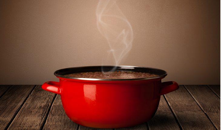 Na foto há uma panela vermelha com alimento dentro soltando uma fumacinha como se o alimento estivesse cozinhando