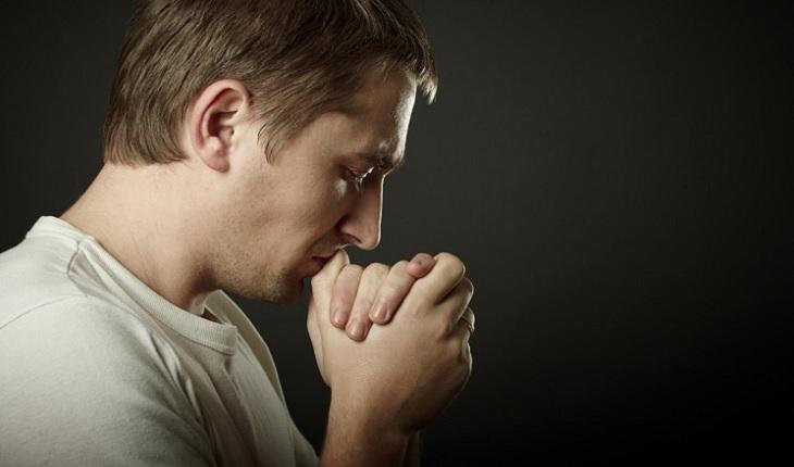 A foto mostra um homem rezando de olhos fechados com as mãos unidas junto ao rosto. O protestantismo é uma doutrina do cristianismo