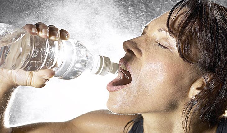 mulher tomando água de uma garrafa de plastico transparente