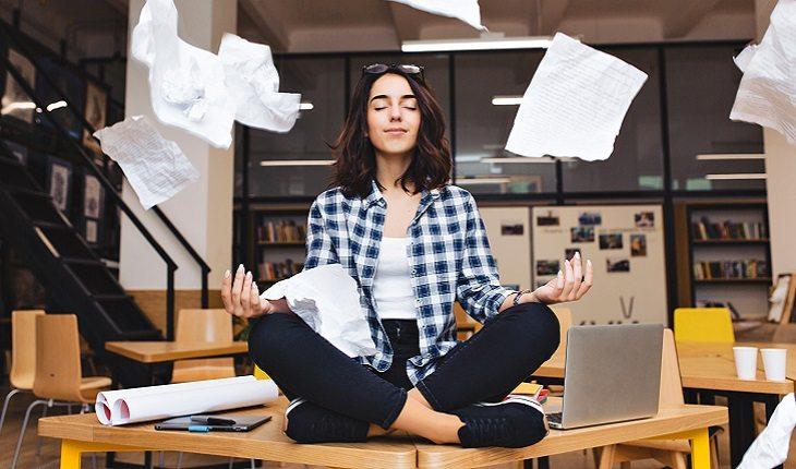 mulher meditando em cima da sua mesa de trabalho enquanto com muitas folhas de papel em volta dela