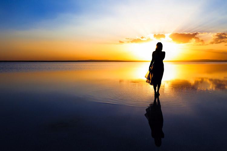 mulher na praia olhando o nascer do sol no mar