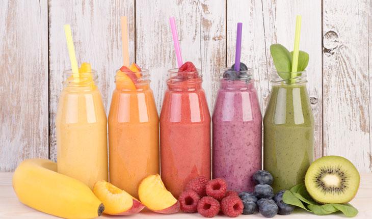 shakes de frutas nas cores amarelo, laranja, vermelho, roxo e verde, servidos em garrafas de vidro com um canudo