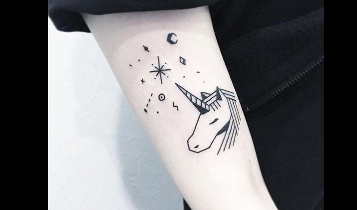 Tatuagem de um unicórnio em preto e branco com detalhes de fogos e luas