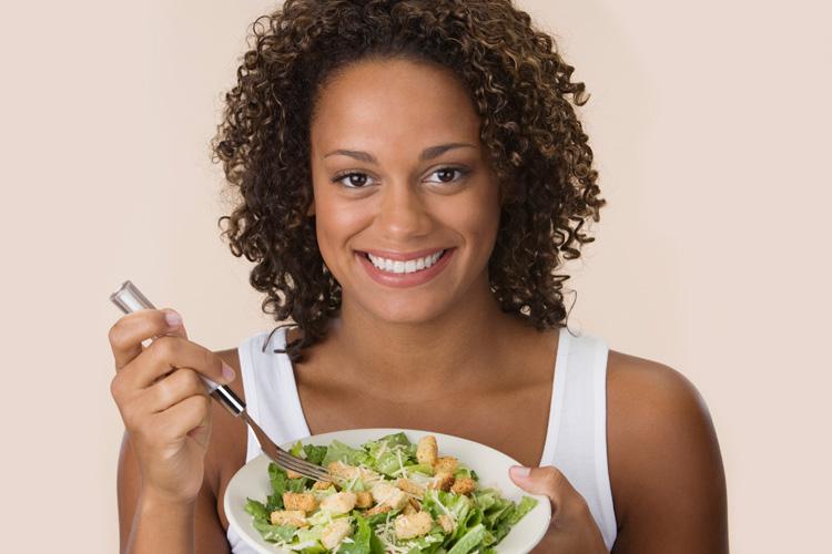 Mulher comendo salada e sorrindo