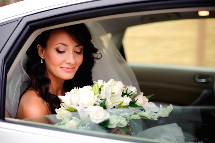 Mulher vestida de noiva espera dentro do carro com buque nas mãos