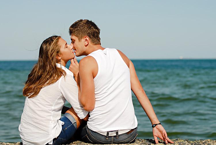 casal se beijando sentados em uma rocha em frente ao mar