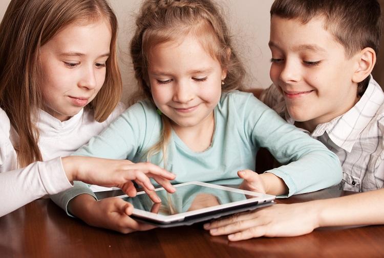 duas meninas e um menino mexendo em um tablet sobre uma mesa, sobre crianças na internet