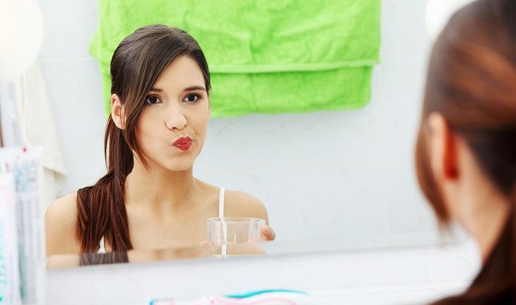 garota olhando no espelho fazendo bochecho com enxaguante bucal