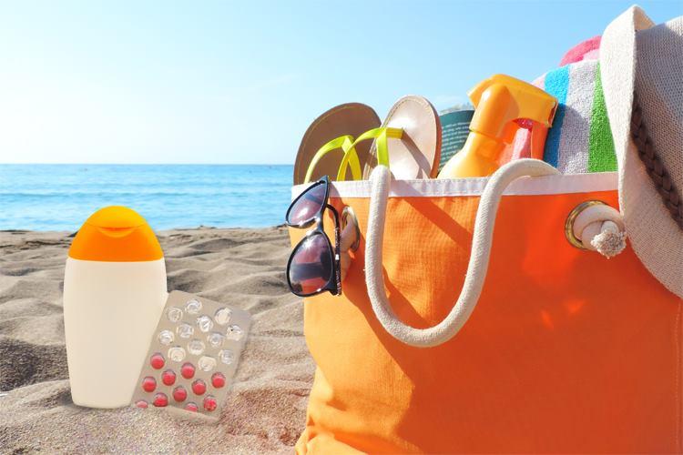 Sacola laranja com chinelo, spray, óculos e outros acessórios de praia. Ao lado, filtro solar de uso tópico e oral. Cenário de praia (filtro solar em cápsulas)