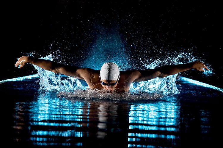 Homem nadando em piscina durante à noite com óculos e touca de natação