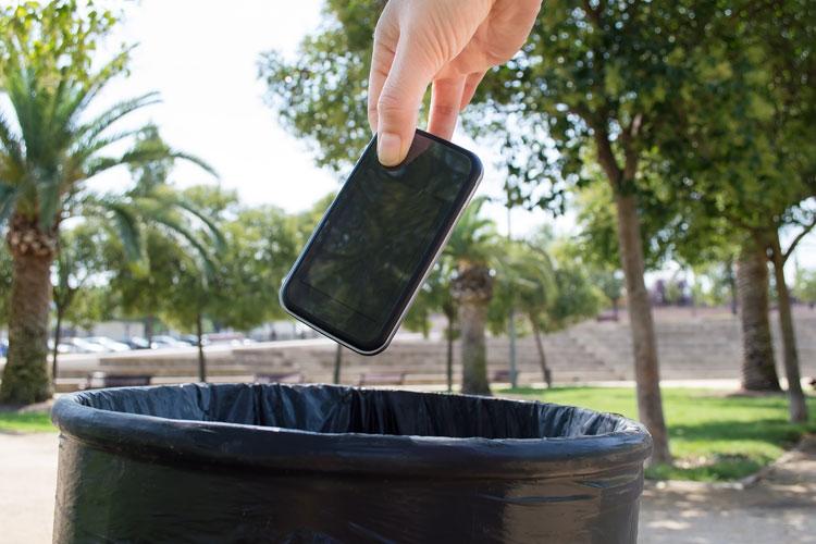 uma mão jogando um celular em um lixo 