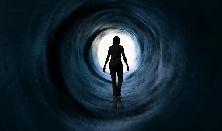 A foto mostra uma mulher andando em direção à luz em um túnel, representando a morte no espiritismo