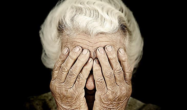 A foto mostra uma mulher idosa coma as mãos no rosto. Catarata