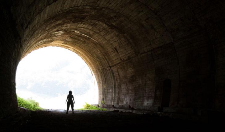 A foto mostra uma mulher na beirada de um túnel, representando a passagem após a morte no espiritismo