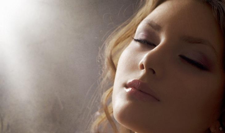 A foto mostra uma mulher rezando com os olhos fechados com uma luz aconchegante em seu rosto, representando a morte no espiritismo