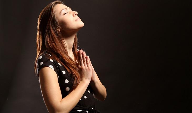 A foto mostra uma mulher de vestido preto rezando ajoelhada. A imagem faz uma alusão à morte no espiritismo