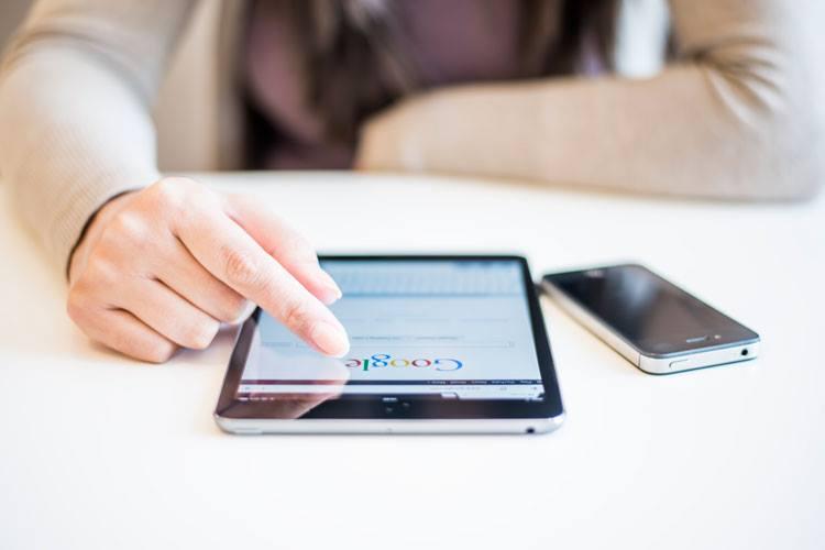 Imagem da mão de uma mulher mexendo na tela de um mini iPad na página do Google