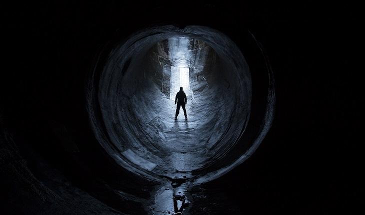 A foto mostra uma pessoa parada em um túnel escuro, fazendo referência à escuridão das pragas