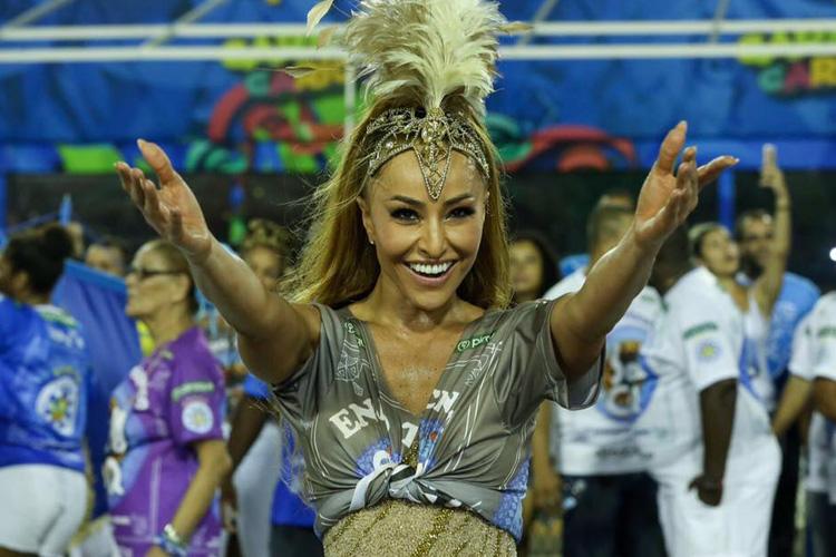 Sabrina Sato de braços abertos e sorrindo em ensaio de escola de samba. Ela veste adereços de Carnaval.