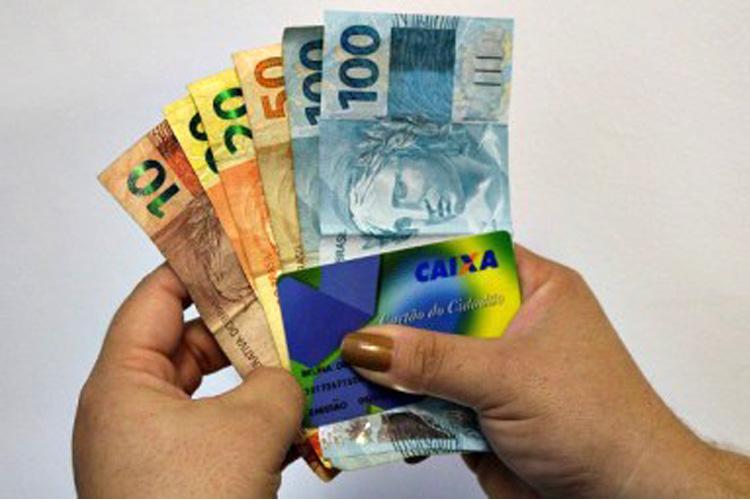 Mãos de mulher segurando notas de dinheiro e o Cartão Cidadão do Brasil (como sacar o FGTS inativo)