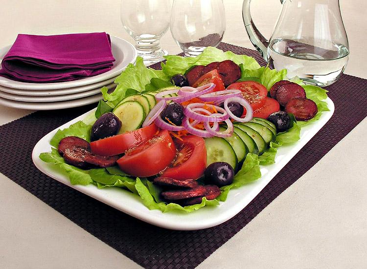 Salada colorida com calabresa em um prato comprido branco sobre uma mesa