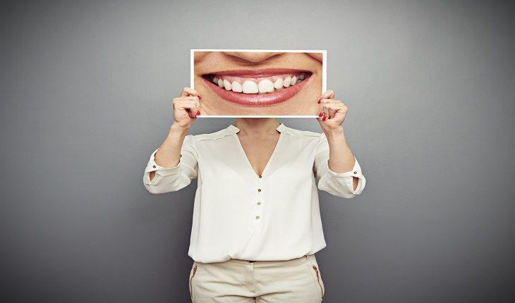 Foto de uma pessoa segurando um cartaz de um sorriso em frente ao rosto